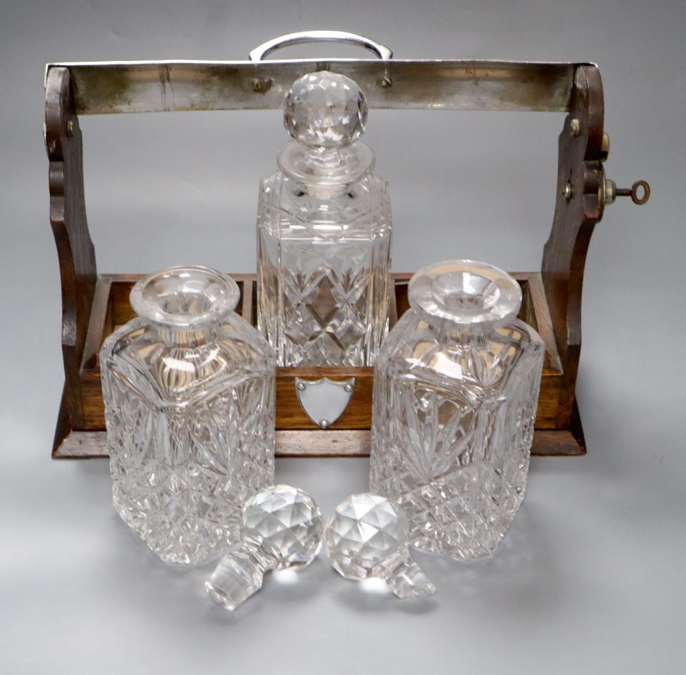 An oak three bottle tantalus, with key, decanters not matching, width 35cm